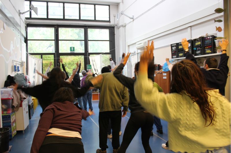 Persone fotografate di spalle danzano all'interno di uno spazio chiuso con finestre.