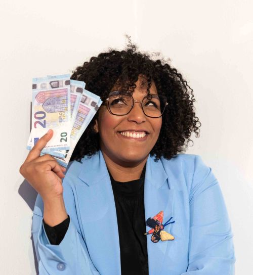 Aminata Gabriella Fall, meglio nota come Pecuniami, è ritratta sorridente e mostra un ventaglio di banconote.