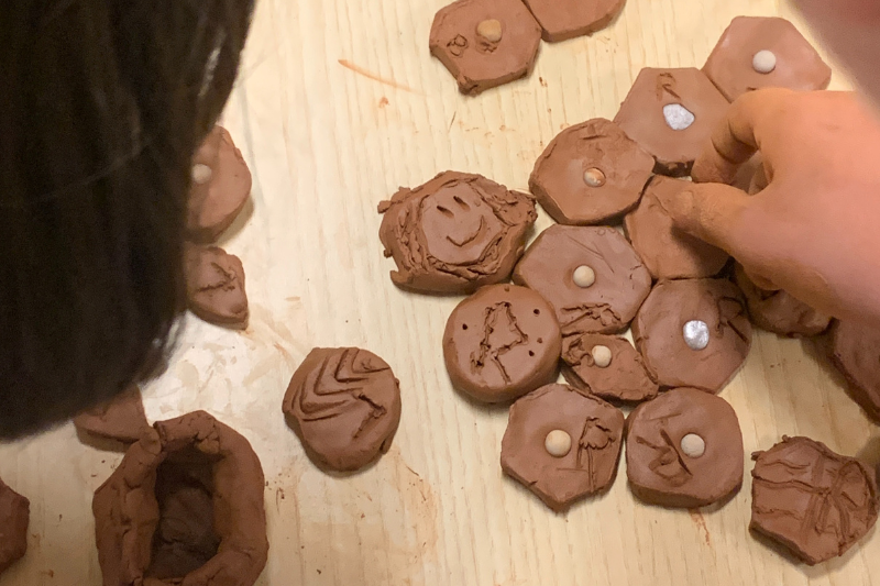 su un tavolo, particolare di una mano di un bambino che compone mosaico in argilla in un laboratorio al museo