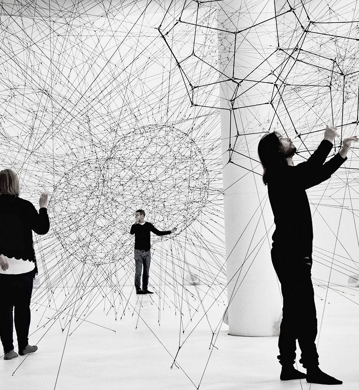 Tre persone vestite di nero osservano con curiosità e toccano forme geometriche in 3d. L'immagine rimanda al mondo dell'innovazione digitale e del 3d.