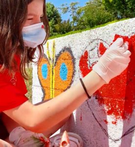 Bambina con una maglia rossa che dipinge un muro con farfalle e un cuore rosso.