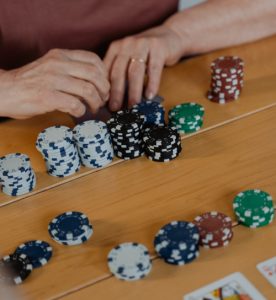 Fiches da poker ordinate su un tavolo di legno. Nell'inquadratura sono presenti solamente le fiches e le mani che le spostano: sono rosse, verdi, bianche, nere e blu.
