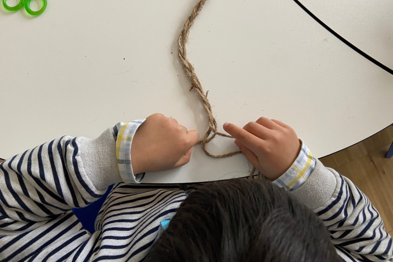 Le mani di un bambino intrecciano una fibra tessile durante un laboratorio didattico al Museo di Claterna.