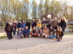 Gruppo di circa 20 persone in posa per la foto su due file. Sullo sfondo degli alberi. Tutte lòe persone indossano una giacce e la giornata è soleggiata.