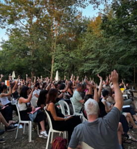 i soci e le socie votano il bilancio 2024 con le mani alzate seduti nel giardino di Maieutica