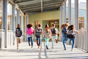 tanti bambini in fila corrono di spalle di fronte all'infresso di una scuola