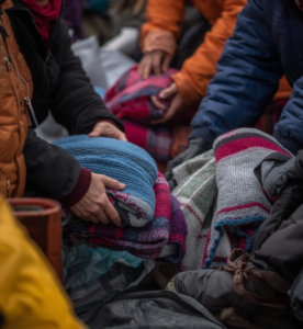 mani e braccia di persone che raccolgono coperte all'aperto con giubbotti per il piano allerte climatiche